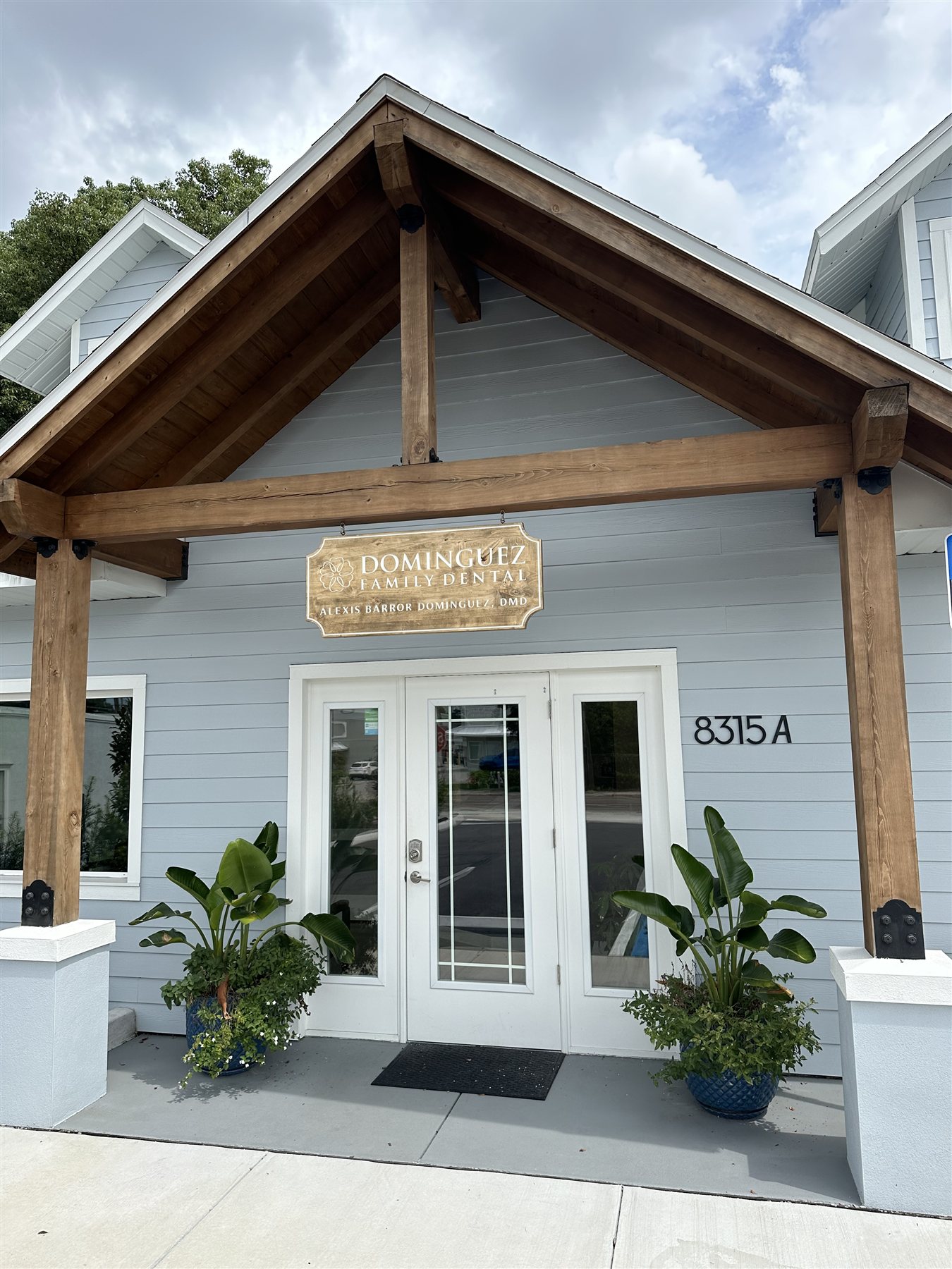 Dominguez Family Dental's entrance, with white doors beneath a wooden canopy and the practice sign.