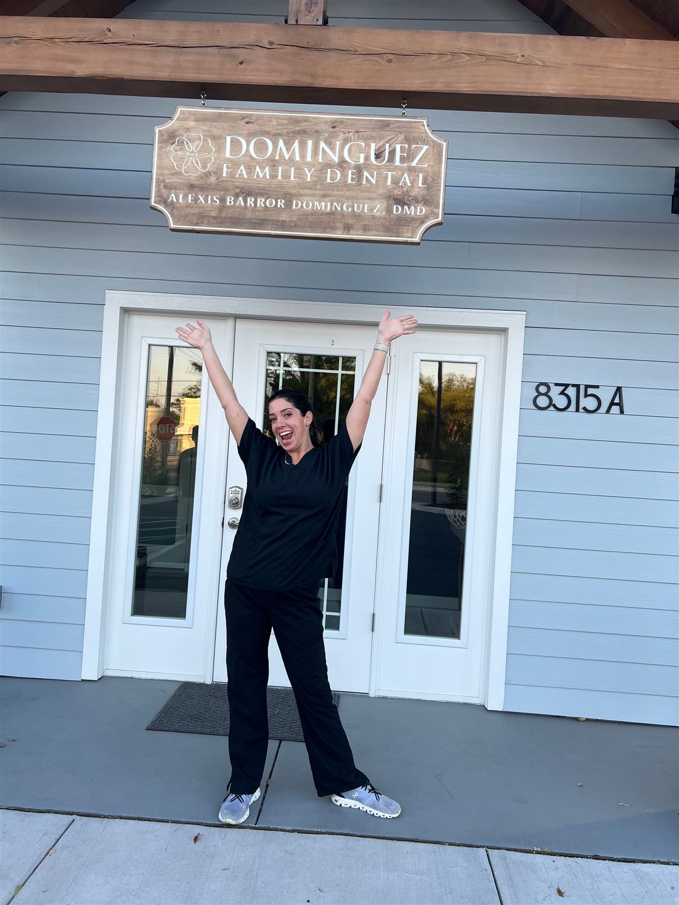 Our dentist smiling in front of the office entrance beneath the Dominguez Family Dental sign.